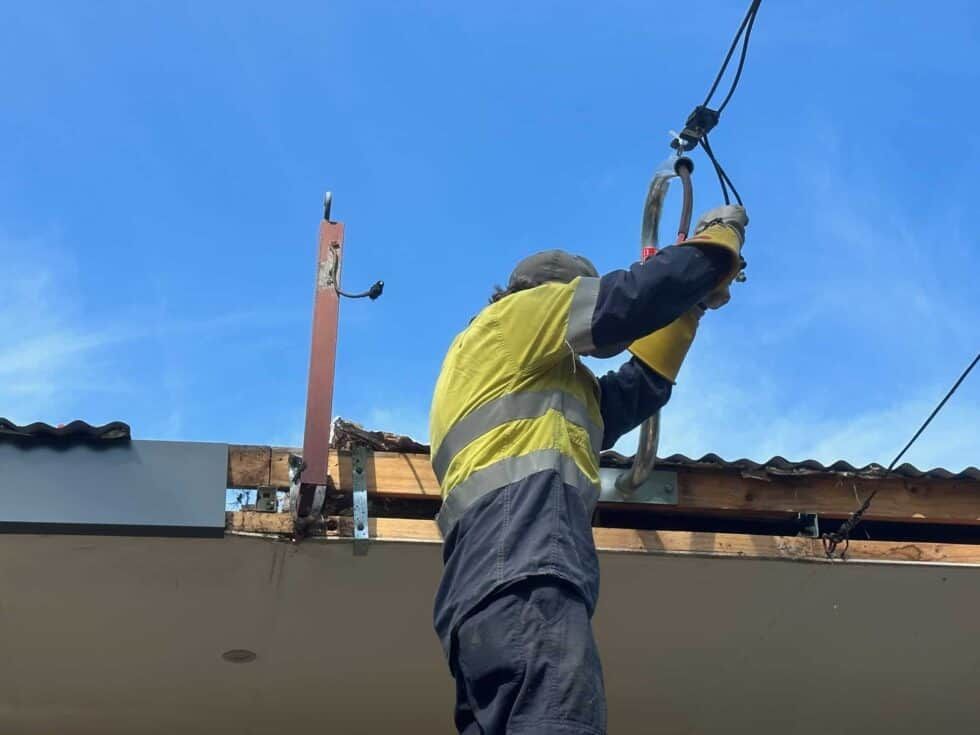 A Man Is Working On A Roof With A Crane — Bay Coast Electrical & Control Solutions in Maloneys Beach, NSW