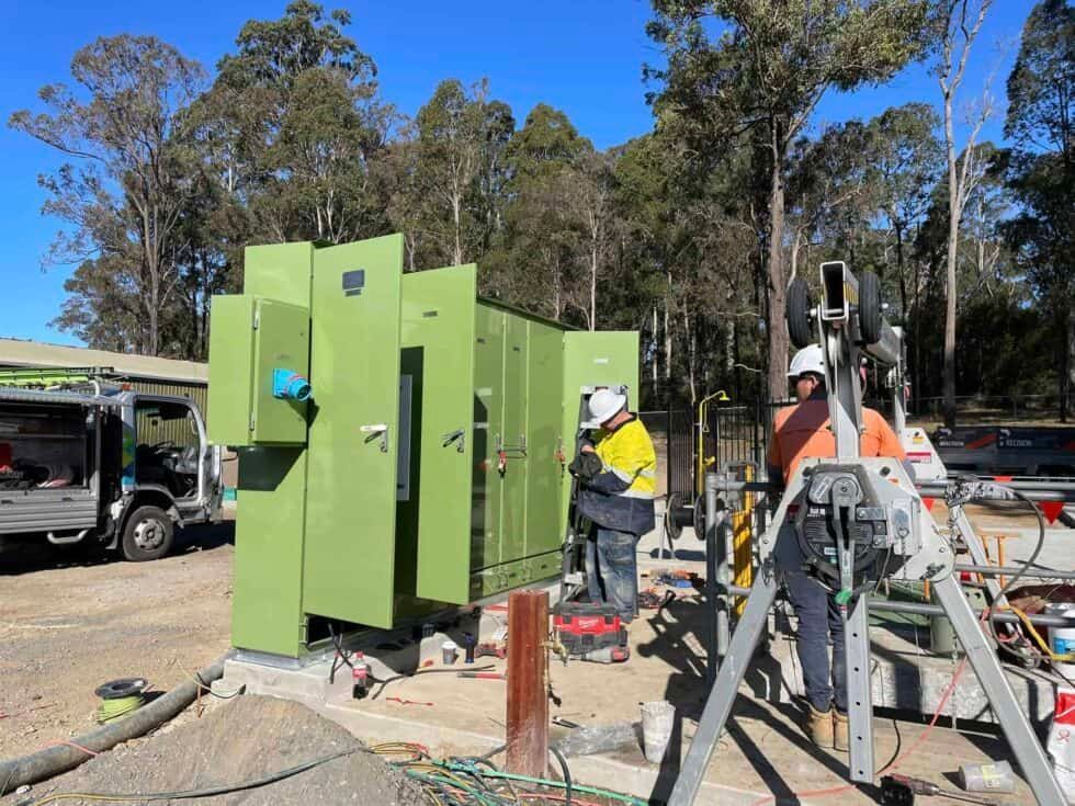 Two Men Are Working On A Green Machine On A Construction Site — Bay Coast Electrical & Control Solutions in Maloneys Beach, NSW