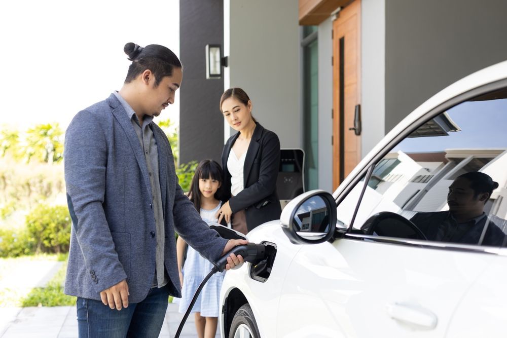 A Man Is Charging An Electric Car With A Charger While A Woman And Child Look On — BayCoast Electrical & Control Solutions In Nelligen, NSW