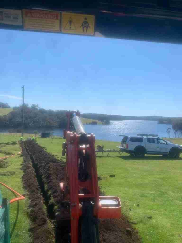 A Tractor Is Digging a Trench in A Field Next to A Lake — Bay Coast Electrical & Control Solutions in Maloneys Beach, NSW