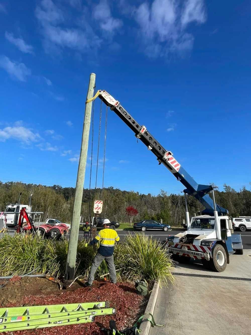 A Crane Is Lifting A Pole In A Parking Lot — BayCoast Electrical & Control Solutions In South Durras, NSW