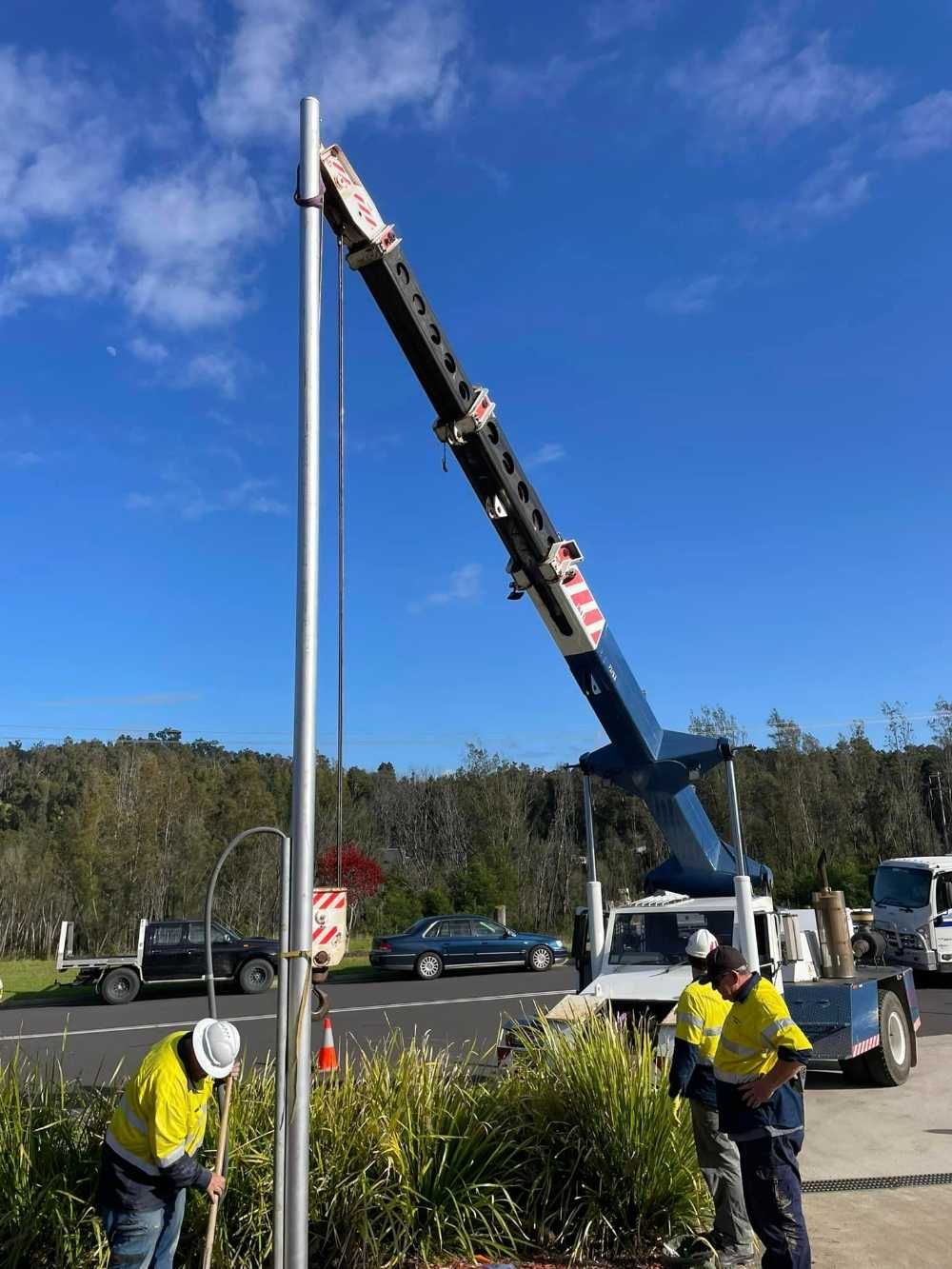 Two Men Are Working On A Pole With A Crane In The Background — BayCoast Electrical & Control Solutions in Sussex Inlet, NSW