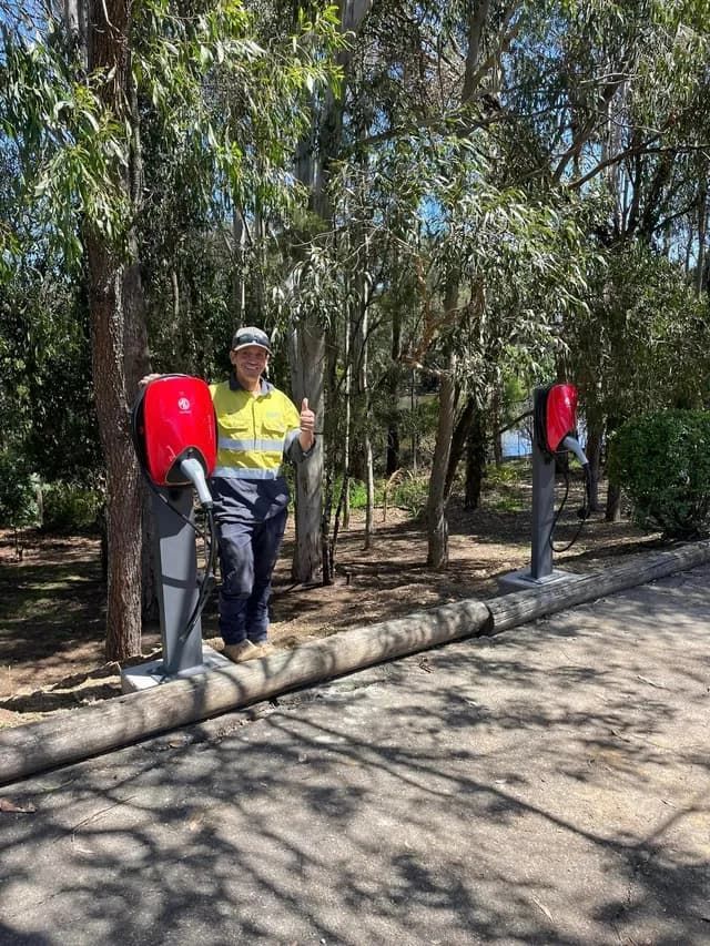 A Man In A Safety Vest Is Standing Next To A Tree In A Park — BayCoast Electrical & Control Solutions in Batemans Bay, NSW