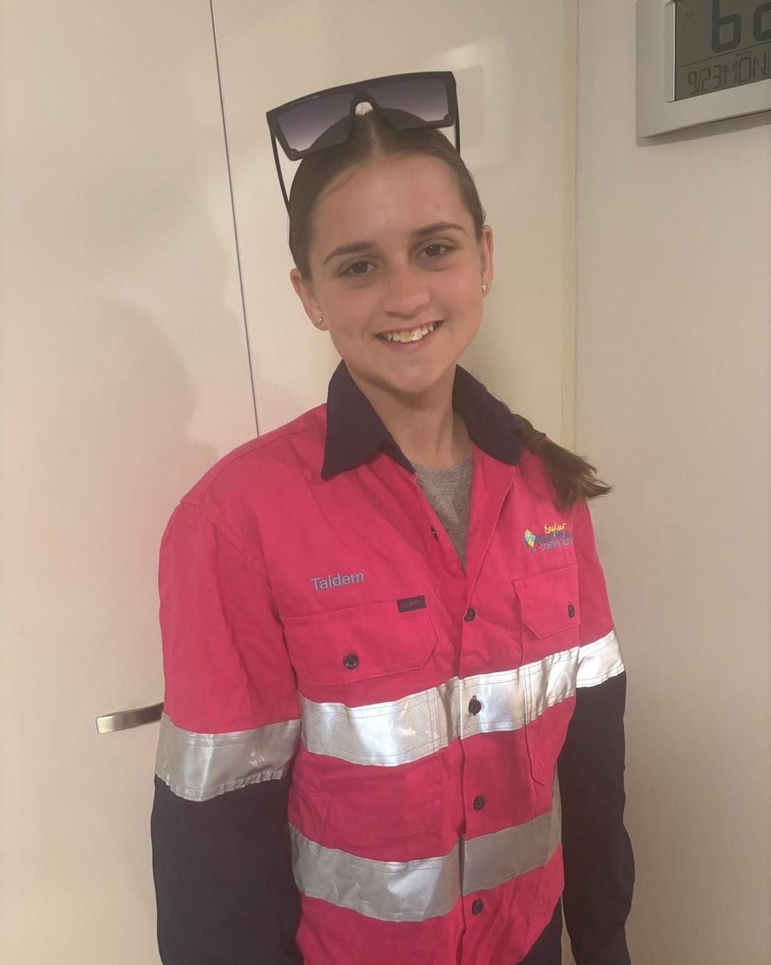Girl smiling, wearing pink work shirt with reflective stripes and sunglasses on head, next to a white door — BayCoast Electrical & Control Solutions in Maloneys Beach, NSW