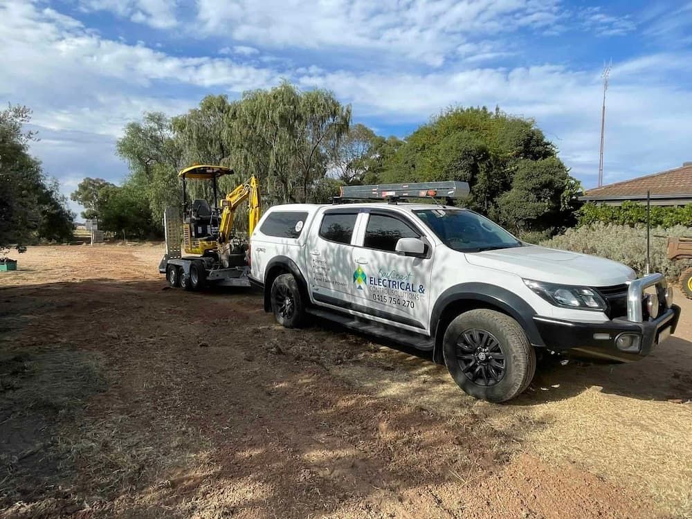 A White Truck Is Towing a Yellow Excavator on A Trailer — Bay Coast Electrical & Control Solutions in Maloneys Beach, NSW