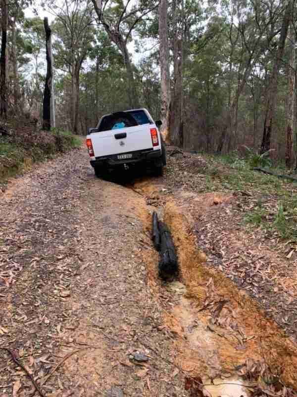 A White Truck Is Stuck in The Mud on A Dirt Road in The Woods — Bay Coast Electrical & Control Solutions in Maloneys Beach, NSW