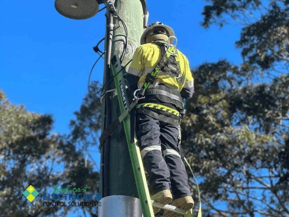 A Man Is Standing on A Ladder Attached to A Pole — Bay Coast Electrical & Control Solutions in Maloneys Beach, NSW