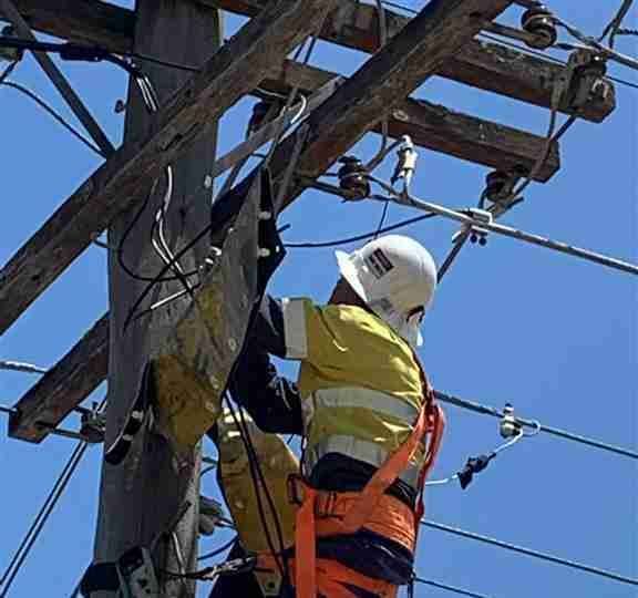 A Man in A Hard Hat Is Working on A Power Line — Bay Coast Electrical & Control Solutions in Maloneys Beach, NSW