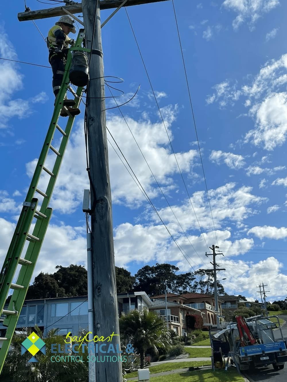 A Man Is Standing on A Ladder on Top of A Power Pole — Bay Coast Electrical & Control Solutions in Maloneys Beach, NSW