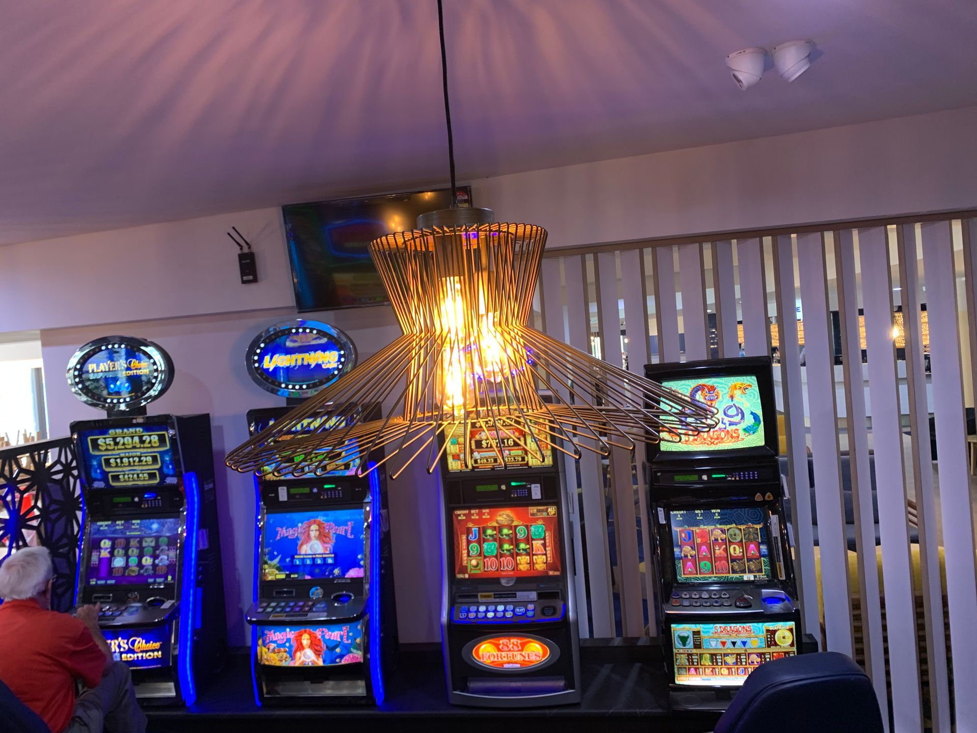A Row Of Slot Machines In A Room With A Chandelier Hanging From The Ceiling — BayCoast Electrical & Control Solutions in Narooma, NSW