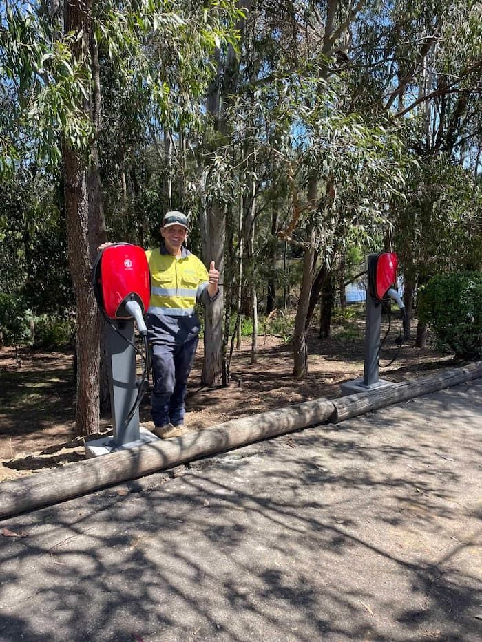 A Man in A Safety Vest Is Standing Next to A Pole in A Park — Bay Coast Electrical & Control Solutions in Maloneys Beach, NSW