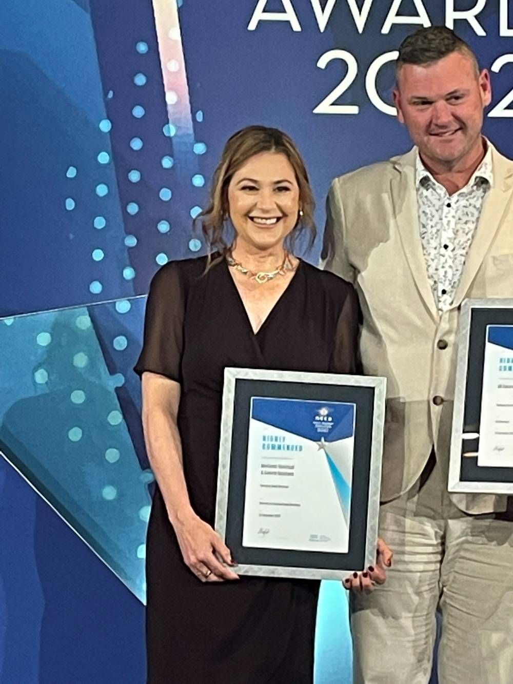 A Man And A Woman Are Posing For A Picture Holding Awards — BayCoast Electrical & Control Solutions in Maloneys Beach, NSW