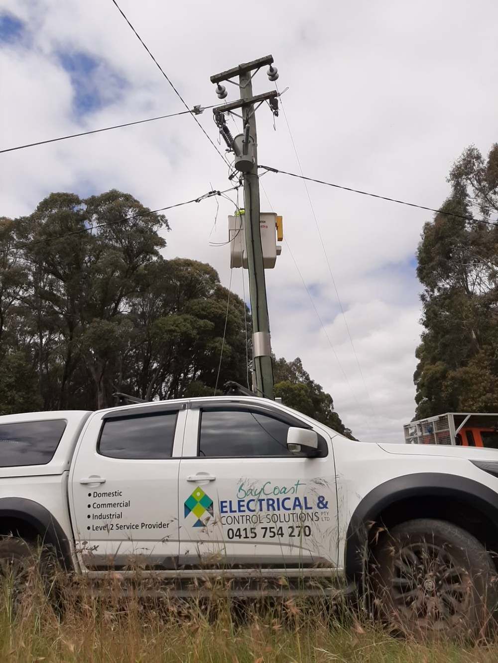 A White Truck Is Parked In A Field Next To A Power Pole — BayCoast Electrical & Control Solutions in Maloneys Beach, NSW