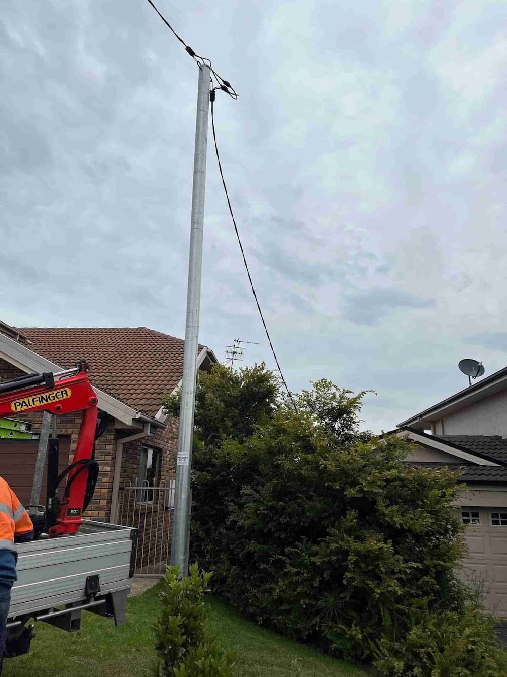 A Man Is Standing Next to A Crane in Front of A House — Bay Coast Electrical & Control Solutions in Maloneys Beach, NSW