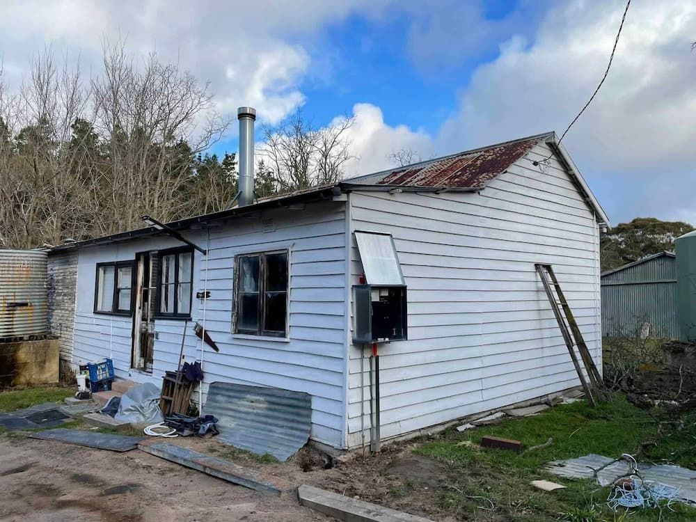 A Small White House Is Sitting in The Middle of A Dirt Field — Bay Coast Electrical & Control Solutions in Maloneys Beach, NSW