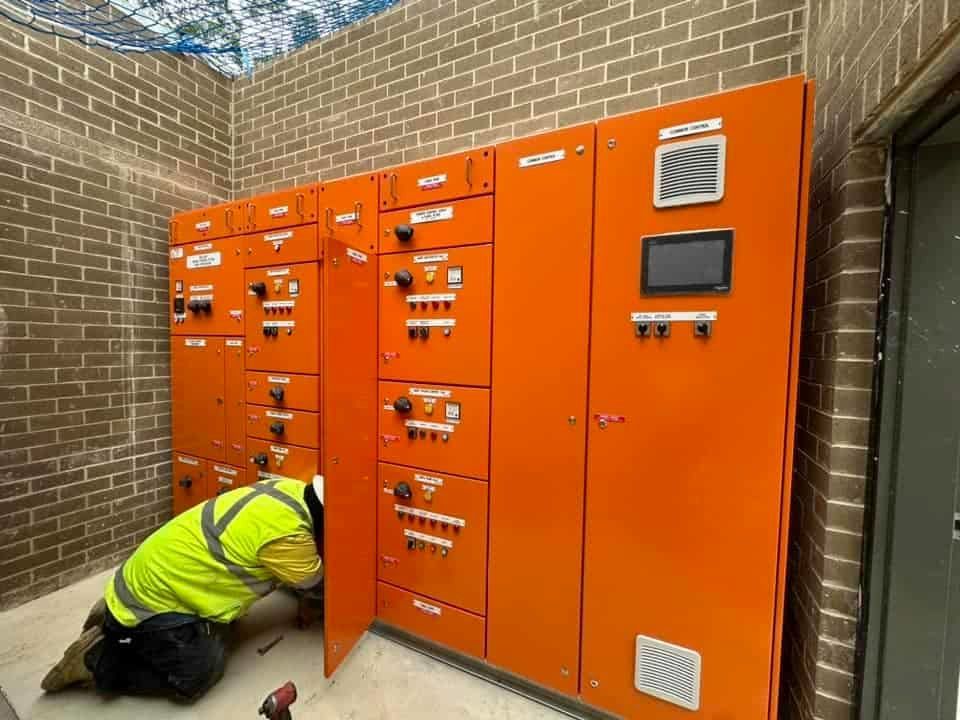 A Man Is Kneeling Down in Front of A Wall of Orange Cabinets — Bay Coast Electrical & Control Solutions in Maloneys Beach, NSW