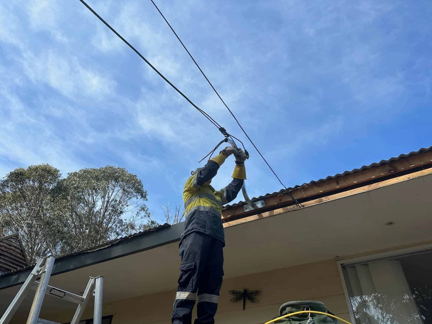 A Man Is Standing on A Ladder on The Roof of A House — Bay Coast Electrical & Control Solutions in Maloneys Beach, NSW