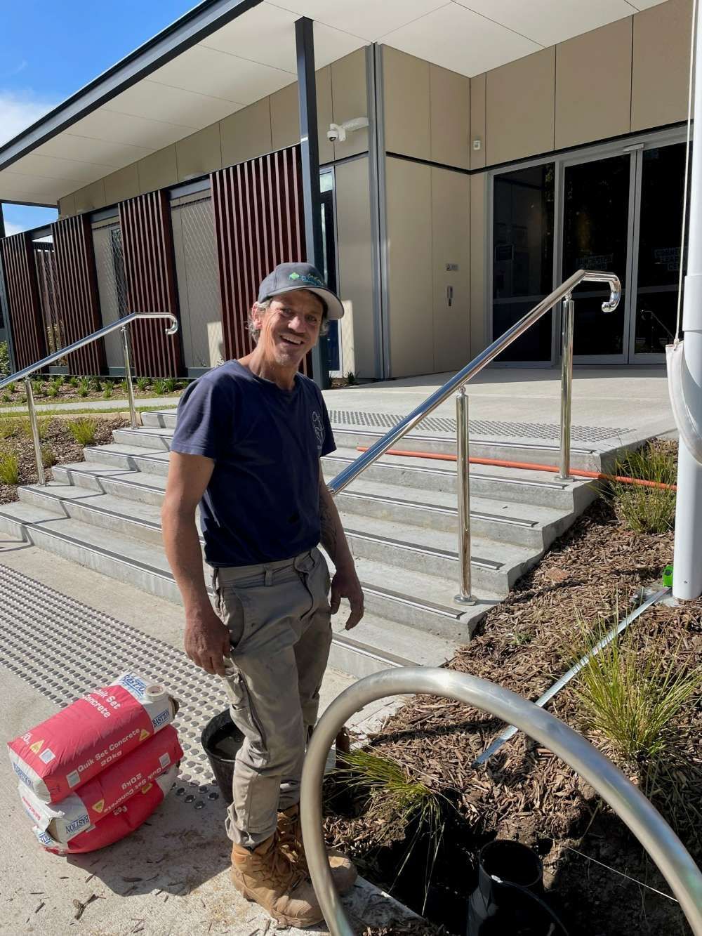 A Man Is Standing In Front Of A Building Next To A Pipe — BayCoast Electrical & Control Solutions in Maloneys Beach, NSW