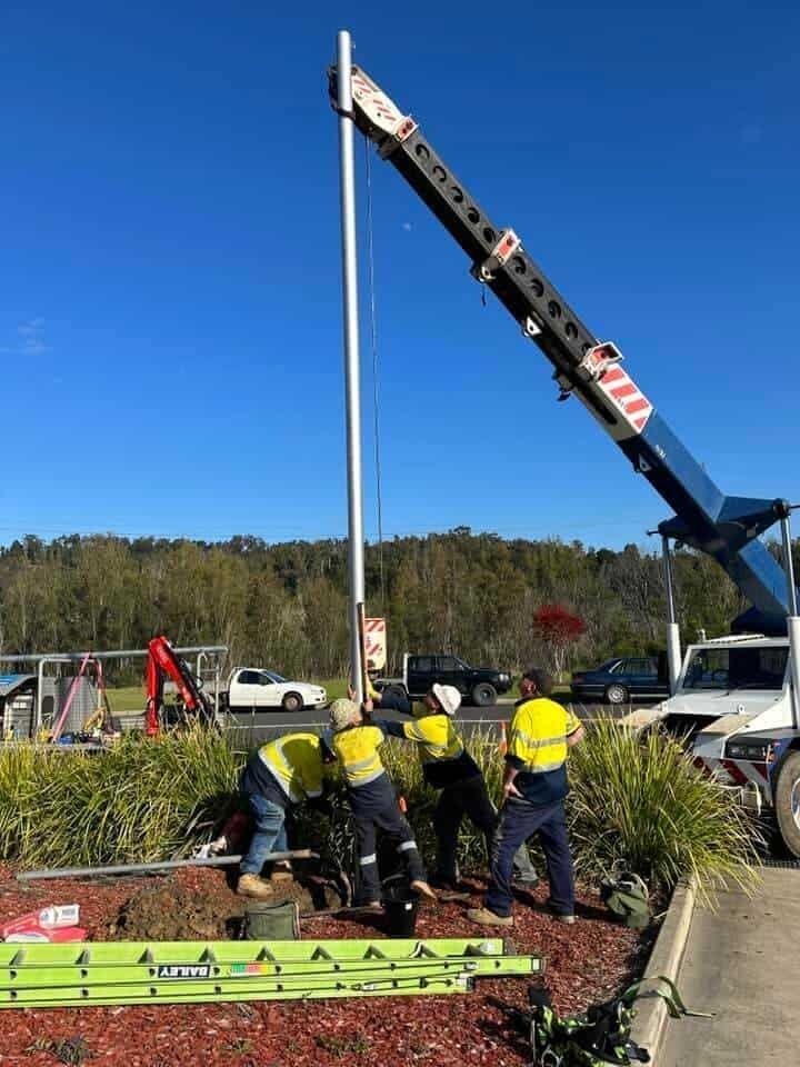 A Group of Construction Workers Are Working on A Pole with A Crane — Bay Coast Electrical & Control Solutions in Maloneys Beach, NSW