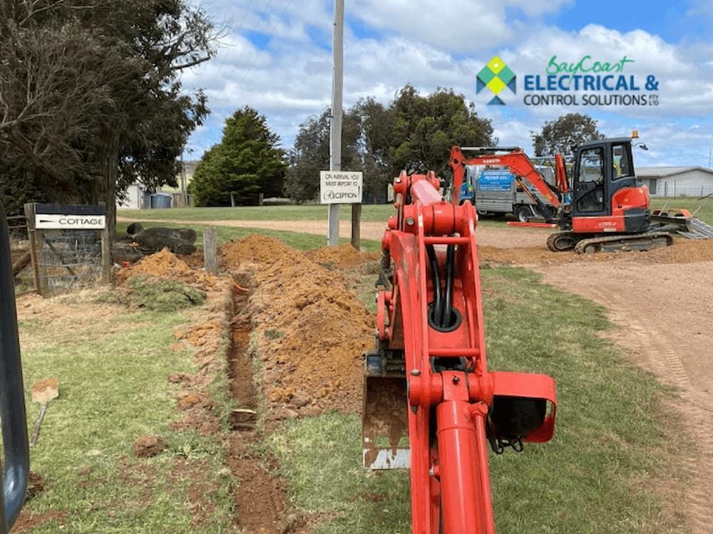 A Red Excavator Is Digging a Hole in The Ground in A Field — Bay Coast Electrical & Control Solutions in Maloneys Beach, NSW