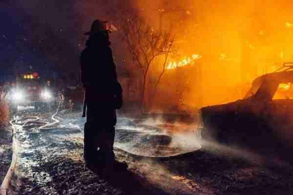 A Firefighter Stands in Front of A Burning Building at Night — Bay Coast Electrical & Control Solutions in Maloneys Beach, NSW