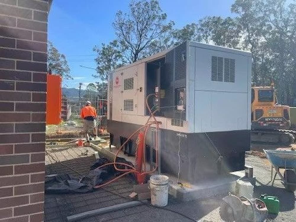 A Man Is Standing Next to A Large Machine on A Construction Site — Bay Coast Electrical & Control Solutions in Maloneys Beach, NSW