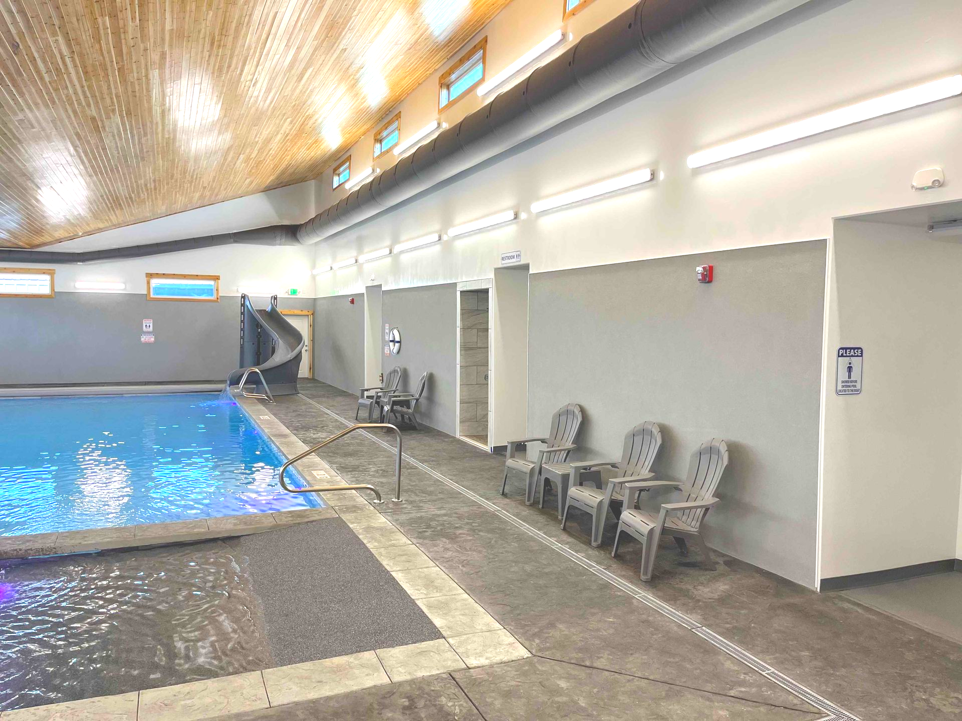 Indoor pool with a water slide, chairs, and a neutral-toned wall.