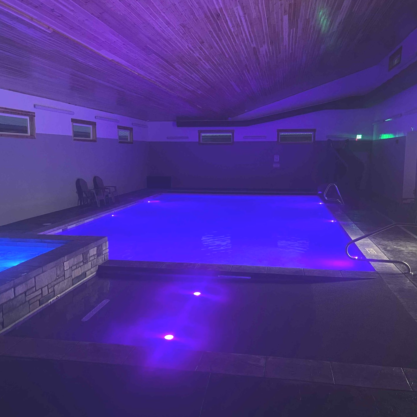 Indoor pool illuminated with blue and purple lights.