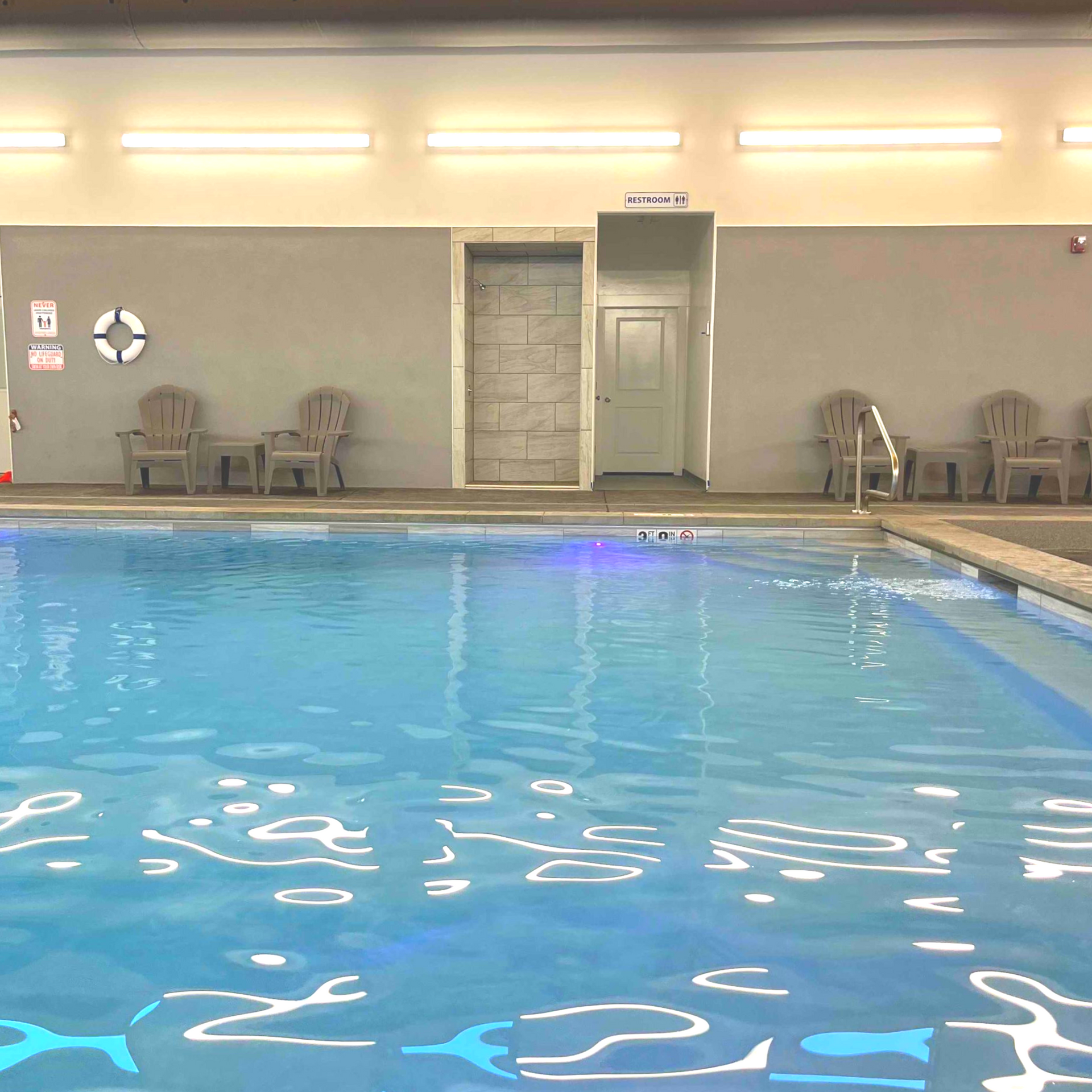 Indoor swimming pool with chairs, a life preserver, and a shower area.