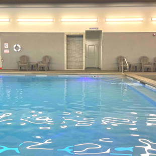 Indoor swimming pool with chairs, a life preserver, and a shower area.