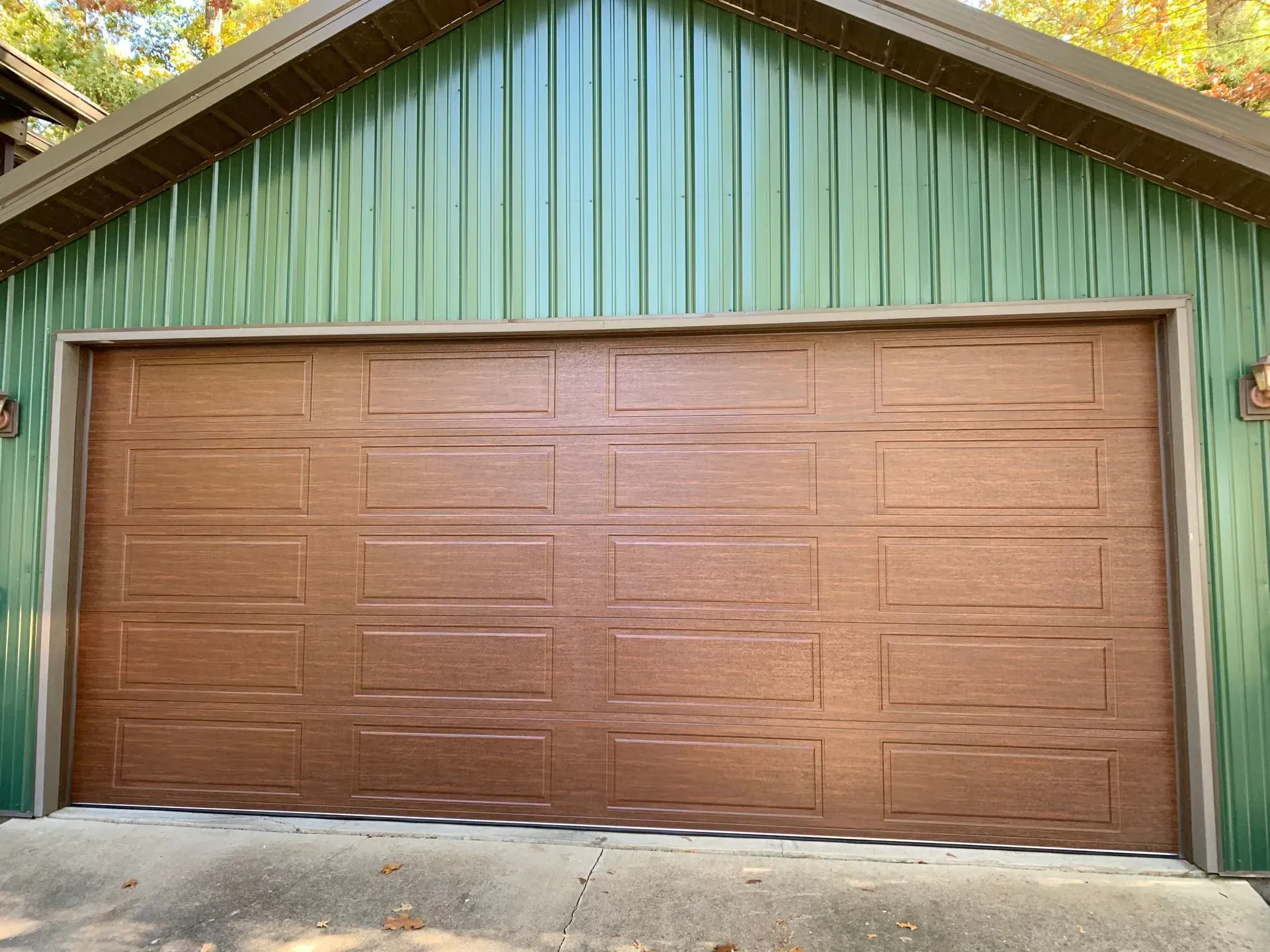 Brown garage door on a green-sided building with a concrete driveway in front.