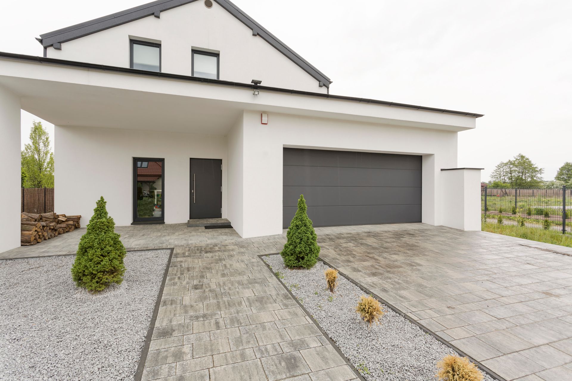 Modern white house with a gray garage, gravel driveway, and small shrubs in front