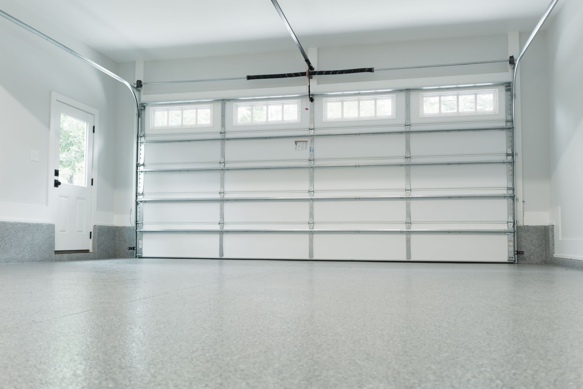 Empty white garage with closed sectional door and speckled floor