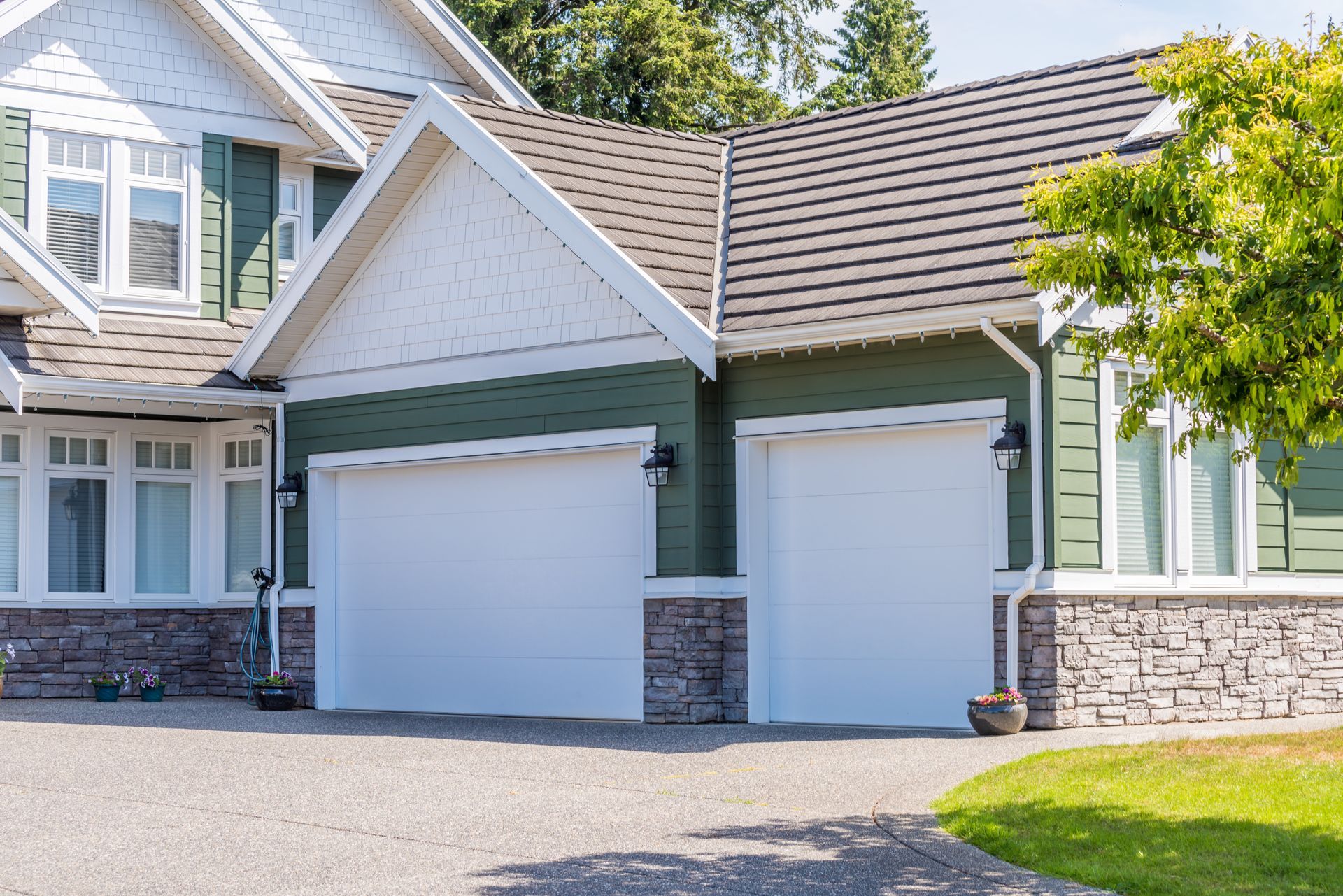 Suburban house exterior with two white garage doors and stone trim under a gabled roof