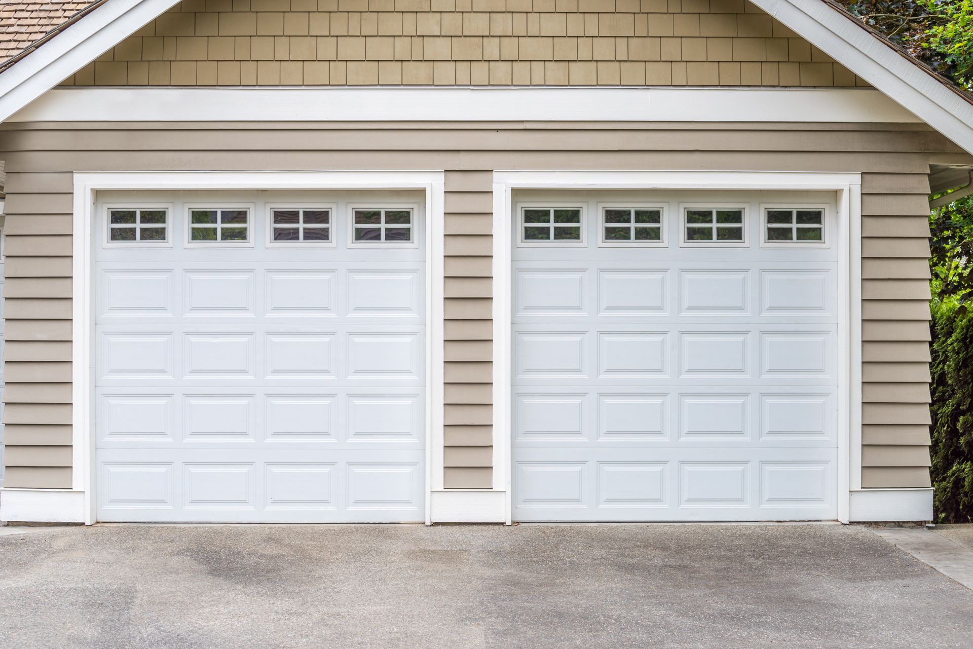 Two white garage doors on a beige house exterior with a gravel driveway in front