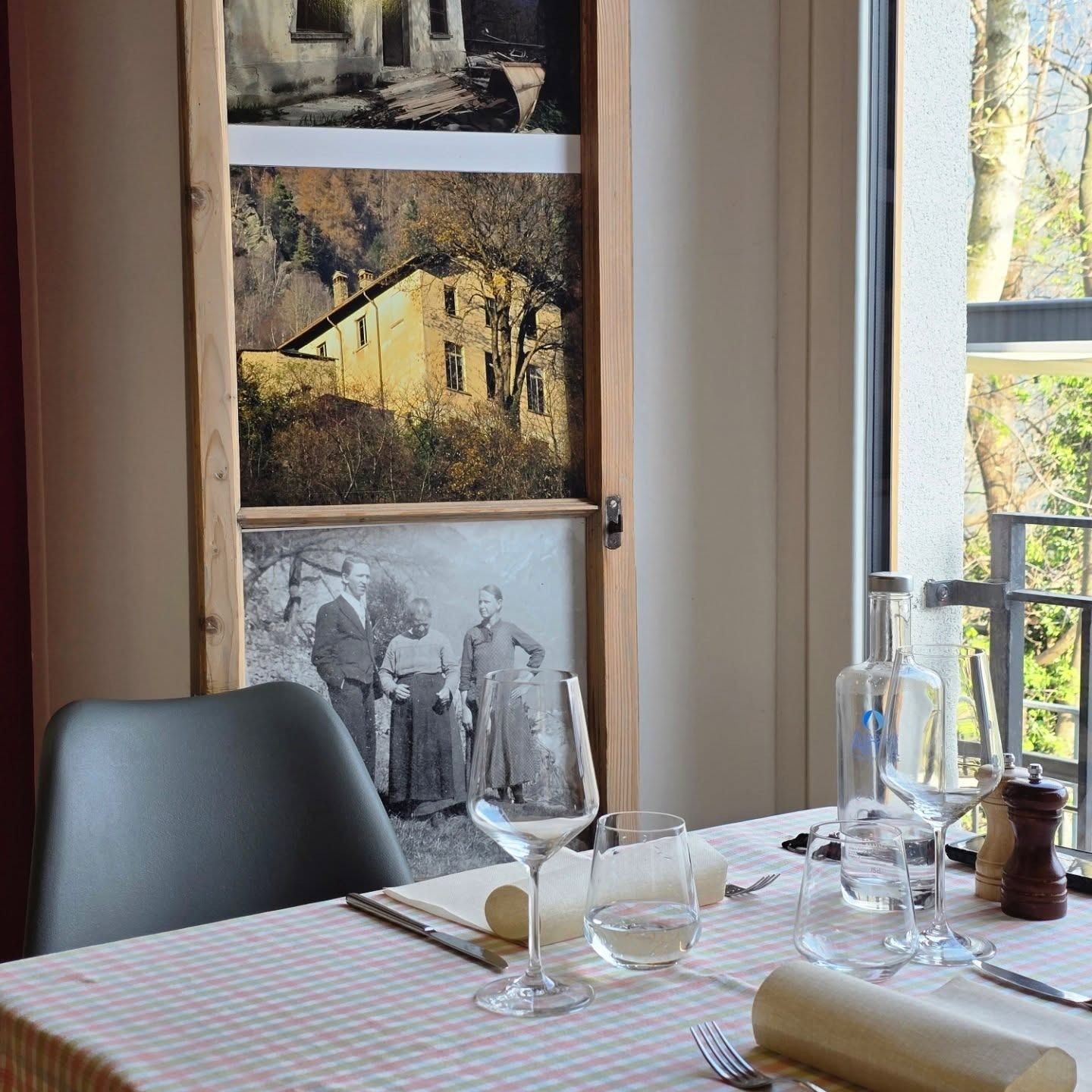 Tavolo del ristorante apparecchiato con bicchieri e vista dalla finestra, un quadro con tre vecchie foto sulla parete.