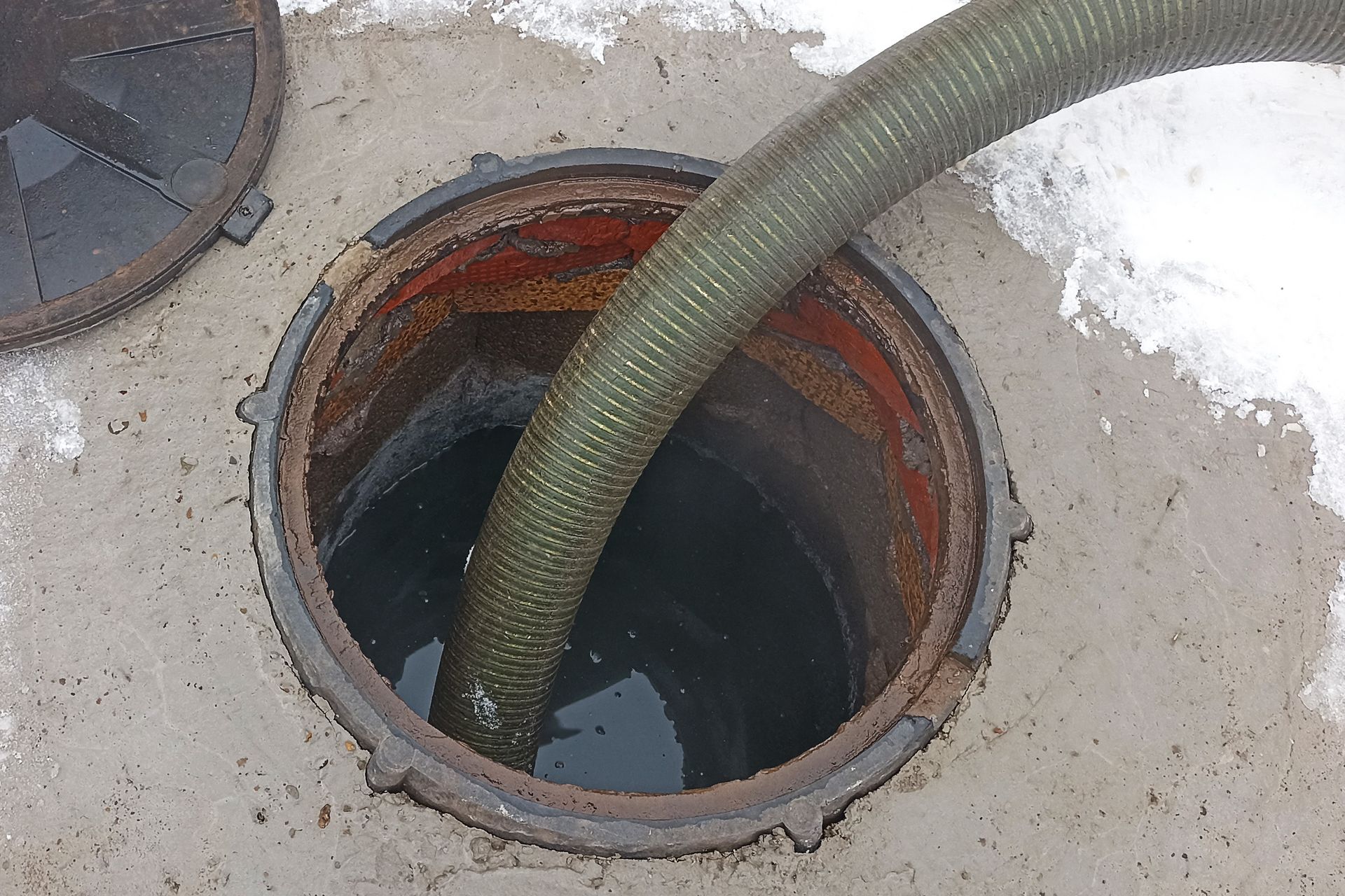 Large hose drains dark liquid from open brick-lined manhole in snow.