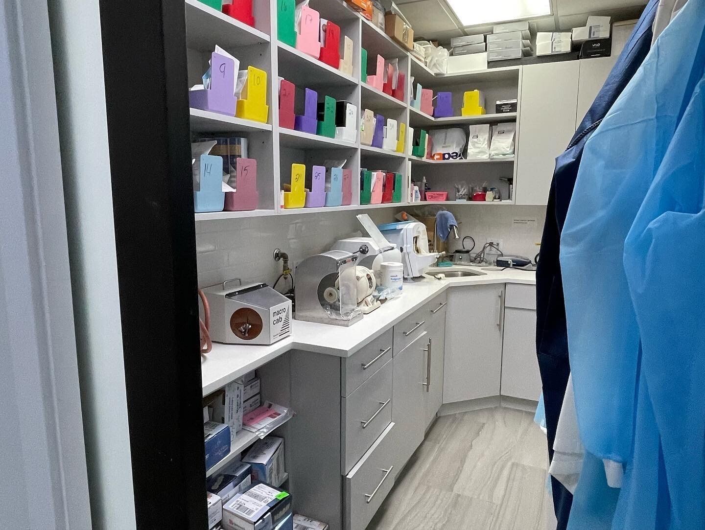 Shelves with colorful boxes and equipment in a medical office, a coat hangs on the right.