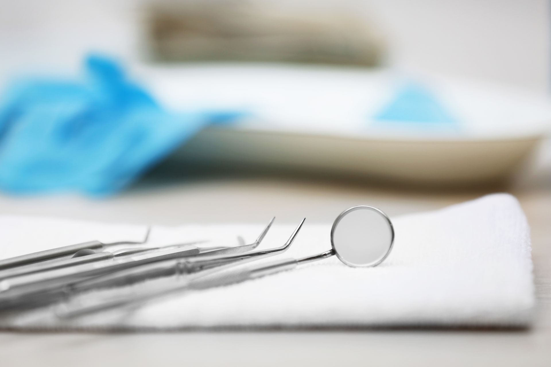 Dental tools rest on a folded cloth in a clean exam area with gloves in the background. Dental tools rest on a folded cloth in a clean exam area with gloves in the background.