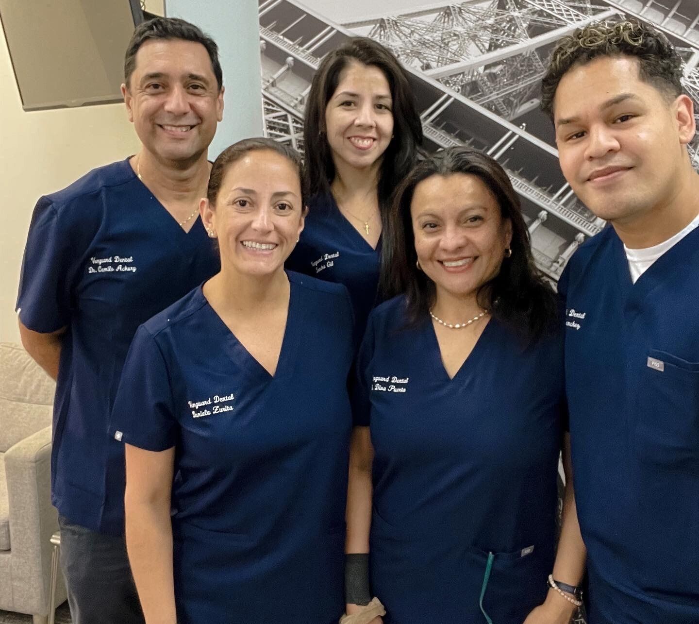 Dental team in blue scrubs, smiling, standing indoors.