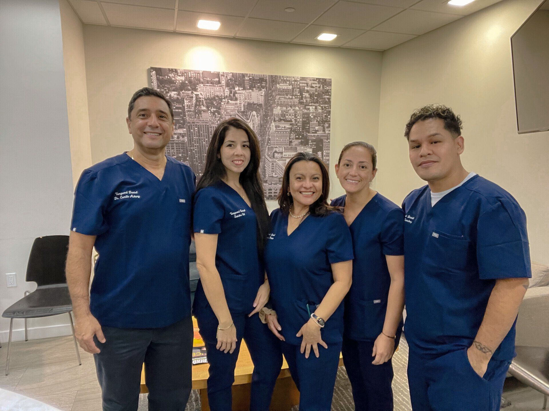 Five people in blue scrubs, smiling, standing in a medical office.