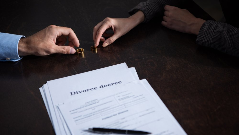 couple placing their wedding rings on a table with divorce papers