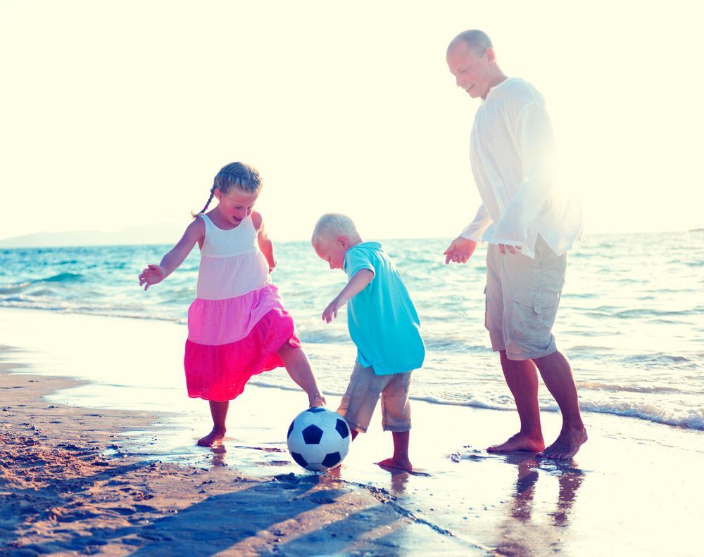 father, daughter, and son playing soccer on the beach