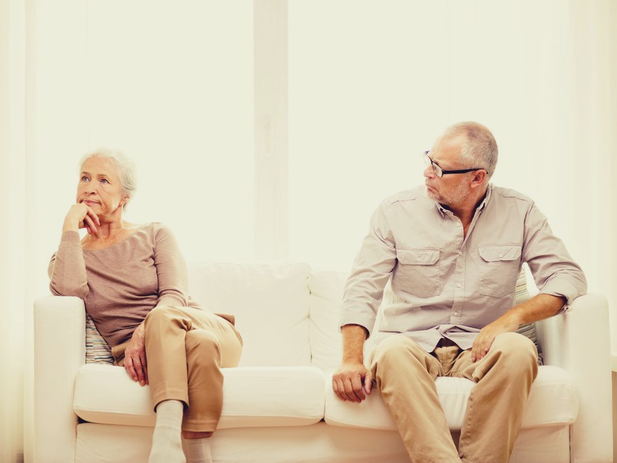 An unhappy older couple sitting apart on a couch