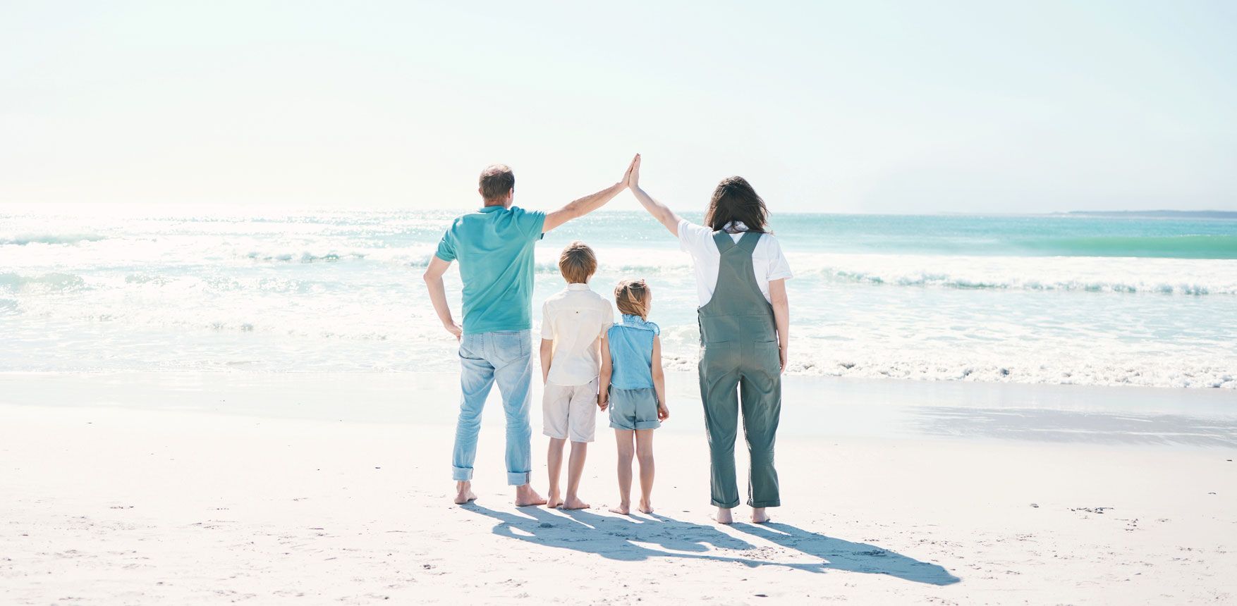 Family of four on a sunny beach, father and mother forming a roof with their hands over the children.
