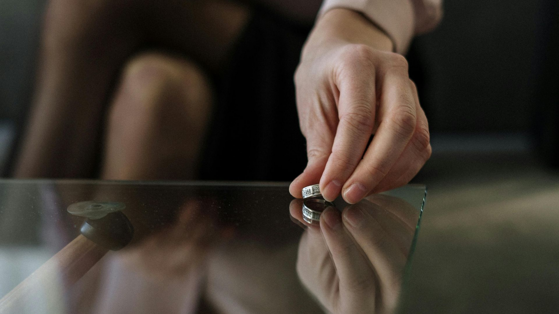 A hand placing a small metal die on a glass table, with its reflection visible.