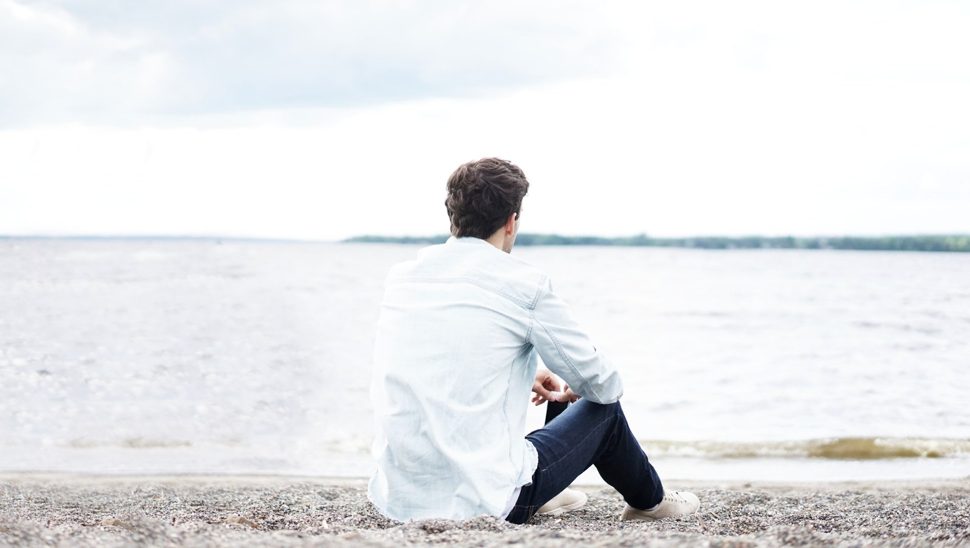 sad man sitting on a lake's shore