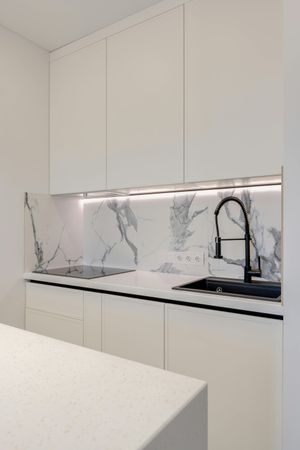 A kitchen with white cabinets , marble counter tops , a sink and a faucet.