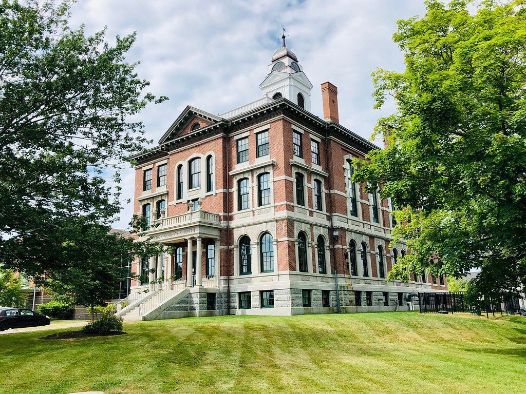 A large brick building with a clock tower is surrounded by trees and grass.