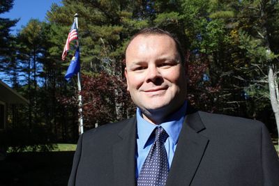 A man wearing a blue shirt and a black vest is smiling for the camera.